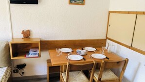 Ein Essbereich mit einem Holztisch, gedeckt für vier Personen, umgeben von Korbstühlen. Eine Regal mit Büchern und einer kleinen Holz-Eichhörnchen-Dekoration befindet sich links.