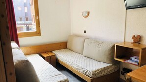 Ein kleines, gemütliches Zimmer mit zwei Holzbett, einem Schlafsofa, einem Fernseher und einer kleinen Holzablage.