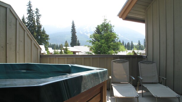 A hot tub on a balcony with two lounge chairs and a view of mountains.