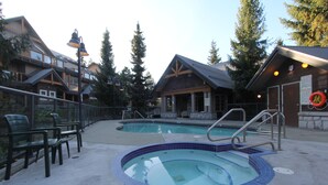 A pool area with two pools, a covered seating area, and a building with a ski lift visible in the background.
