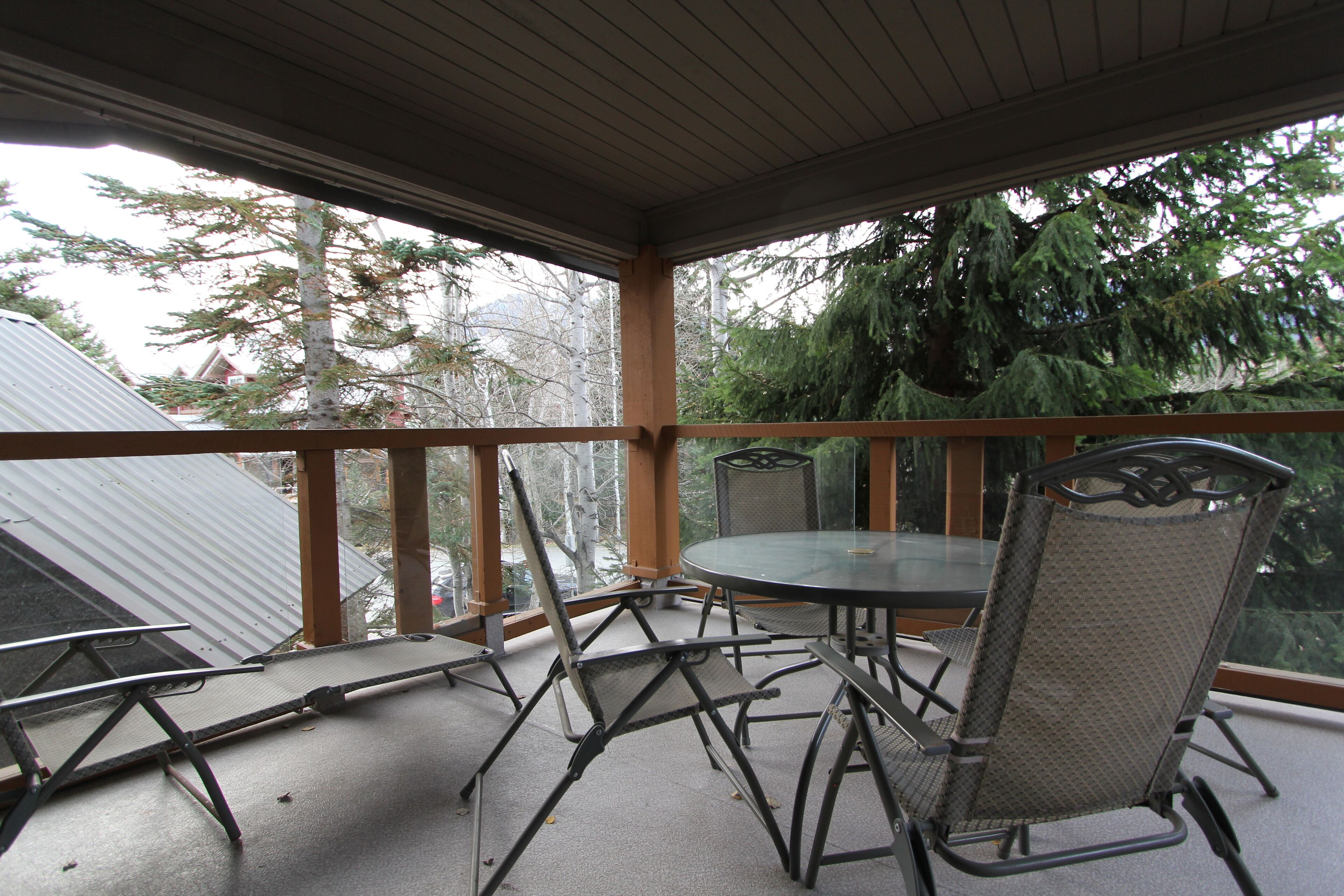 A covered outdoor patio with a table and chairs, surrounded by trees.