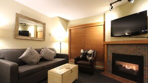 A living room with a sofa, armchair, coffee table, fireplace, TV, and a mirror.