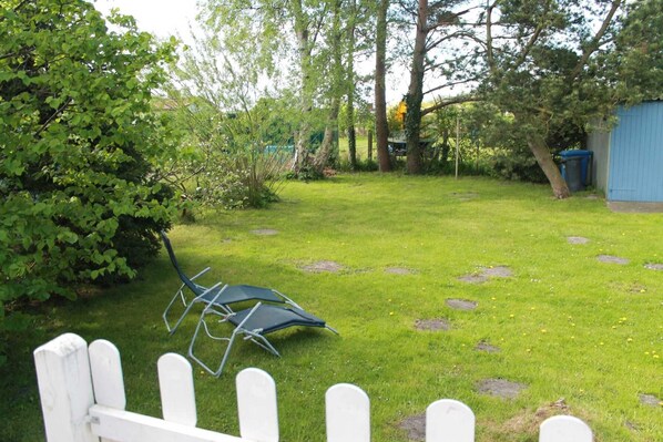 A grassy yard with a white picket fence, a blue shed, and a metal chair.