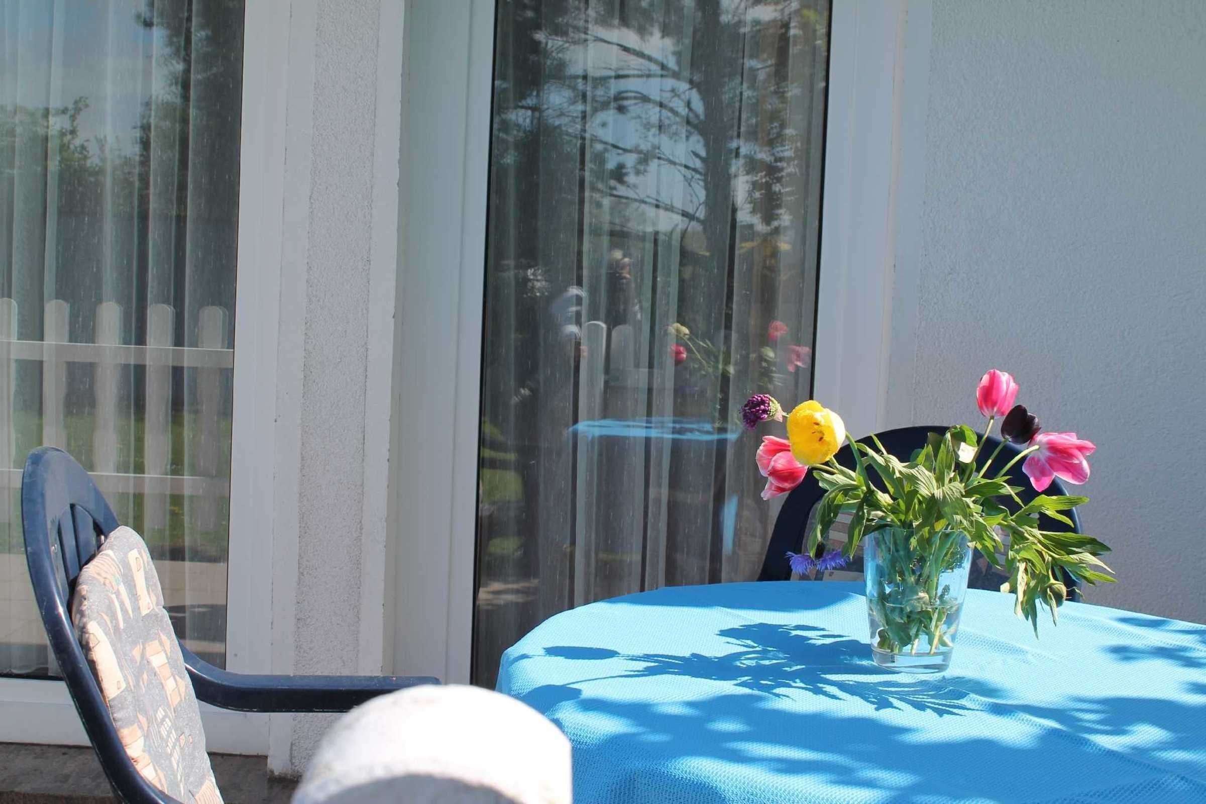 Une table recouverte d’une nappe bleue, une chaise et un vase rempli de fleurs.
