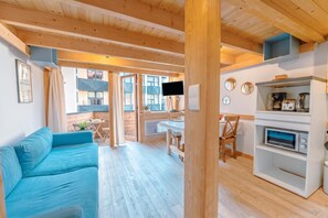 Un intérieur moderne avec un canapé bleu, un plafond en bois et un coin cuisine équipé d’appareils électroménagers.