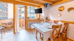 A wooden interior with a dining area, a TV mounted on the wall, and a view through the glass door. - Grand Roc C322 280m from Slopes, Parking & WiFi, Argentière (Chamonix), France (Argentière (Chamonix))