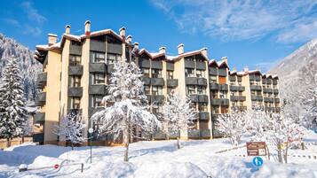 Un hôtel à plusieurs étages, doté de balcons, bordé d’arbres couverts de neige et surplombant un ciel bleu azur.
