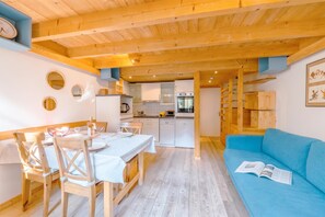 Une cuisine moderne avec des meubles blancs, une table à manger pour deux personnes et un canapé bleu dans l’espace salon.