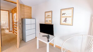 A room with a white desk, a flat-screen TV, a white chair, and two framed pictures on the wall. - Grand Roc C322 280m from Slopes, Parking & WiFi, Argentière (Chamonix), France (Argentière (Chamonix))