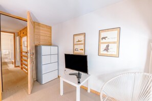 A room with a white desk, a flat-screen TV, a white chair, and two framed pictures on the wall. - Grand Roc C322 280m from Slopes, Parking & WiFi, Argentière (Chamonix), France (Argentière (Chamonix))