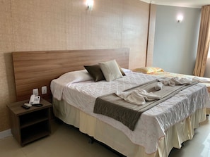 A neatly made bed with a wooden headboard, a bedside table with a phone and a remote control, and a wall-mounted light fixture. - Beira Mar Hotel (Aracaju)