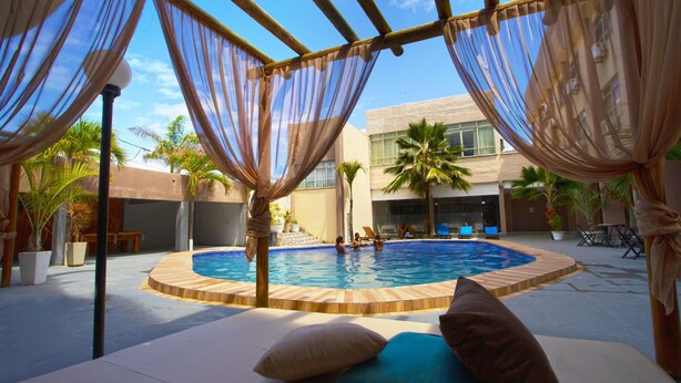 An outdoor pool area with a wooden deck, lounge chairs, and a covered seating area with sheer curtains. - Beira Mar Hotel (Aracaju)