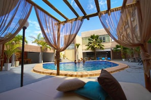 An outdoor pool area with a wooden deck, lounge chairs, and a covered seating area with sheer curtains. - Beira Mar Hotel (Aracaju)