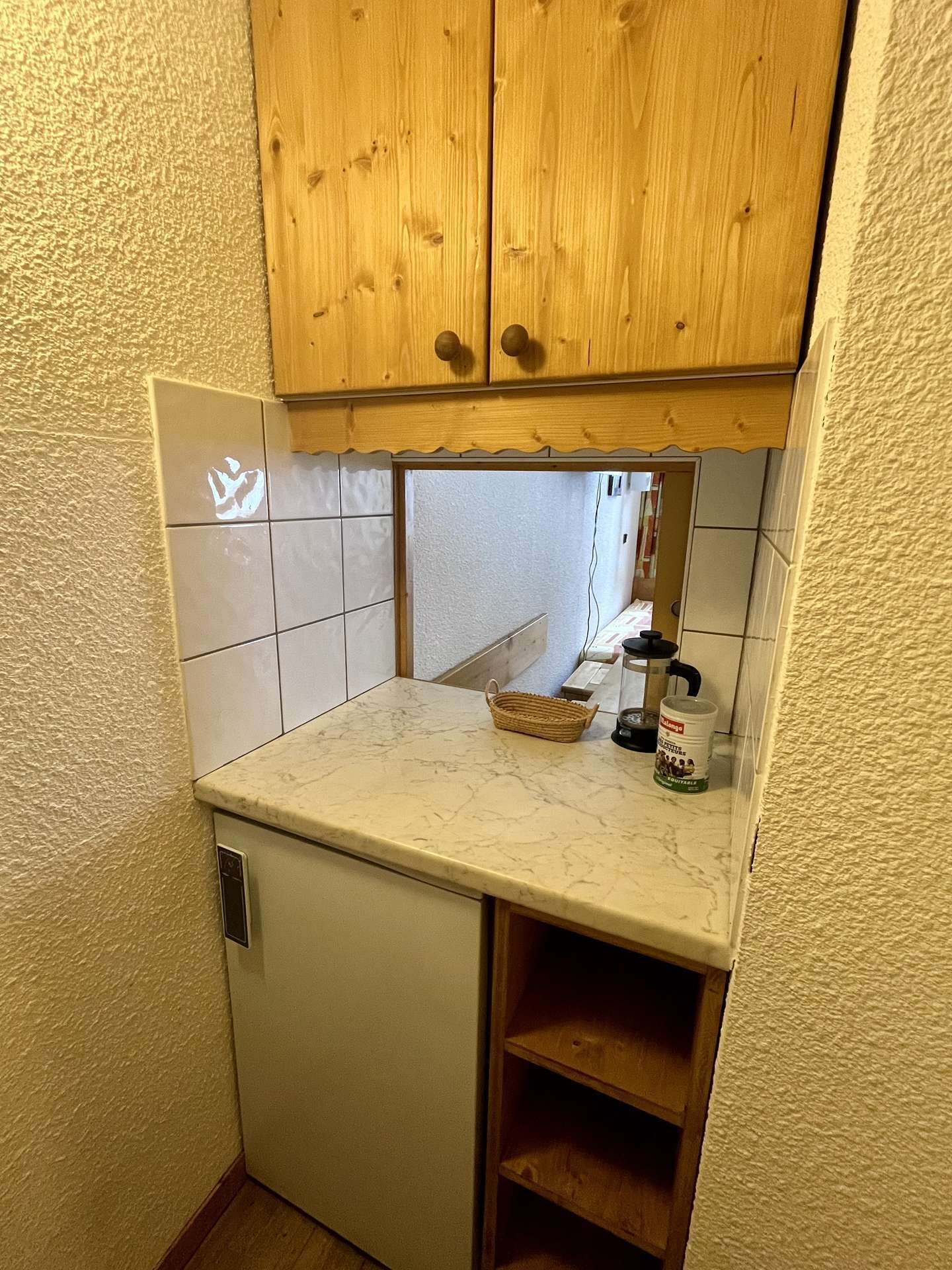 Una cocina compacta con un refrigerador pequeño, armarios de madera, encimera de mármol y salpicadero de azulejos.