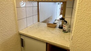 Una cocina compacta con un refrigerador pequeño, armarios de madera, encimera de mármol y salpicadero de azulejos.