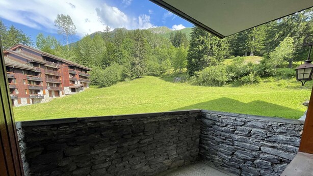 Un balcón con muros de piedra, vistas a un césped verde y un edificio al fondo.
