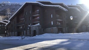 Una cabaña de varios pisos con balcones y una entrada de piedra, rodeada de nieve.