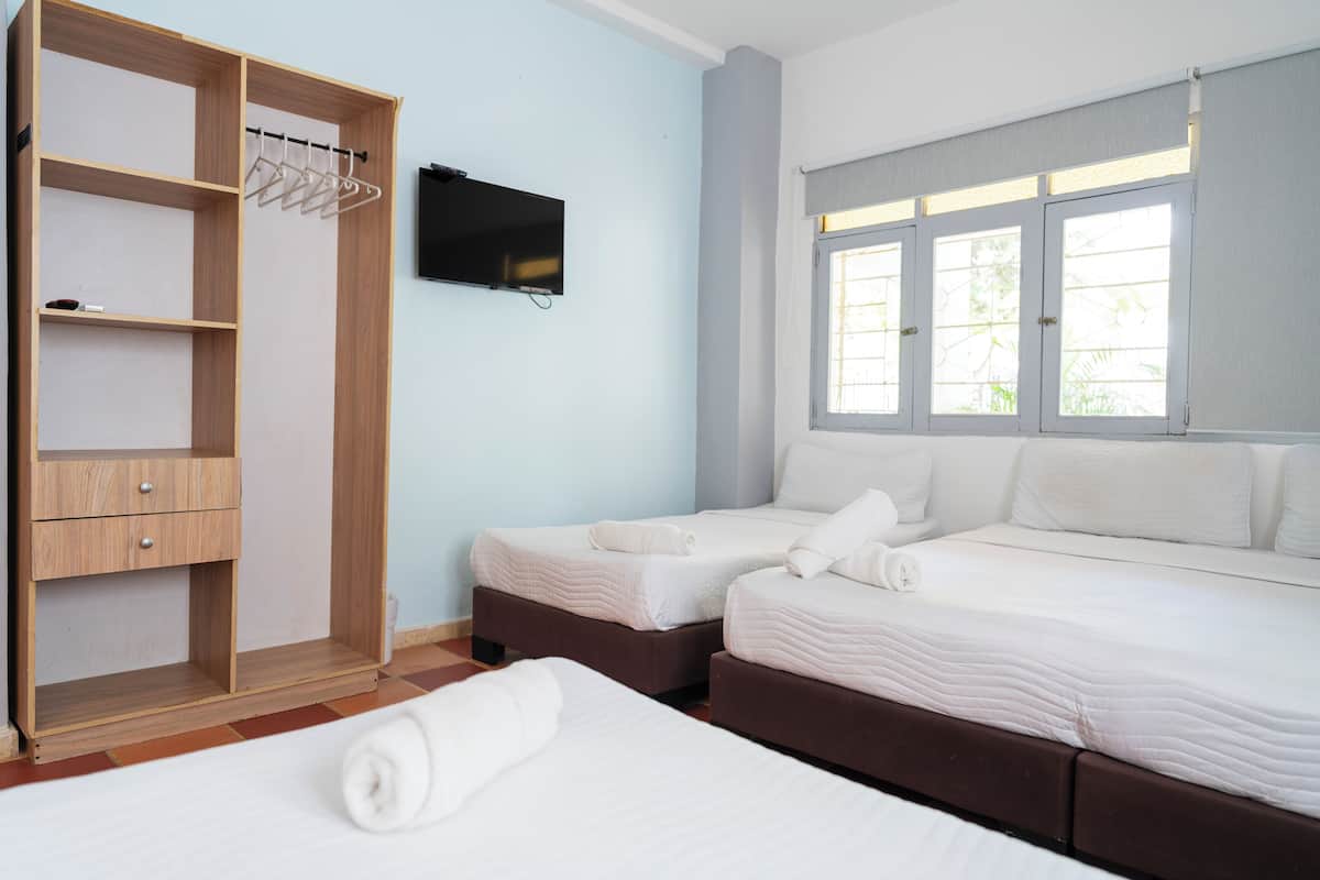 A hotel room with two beds, a wooden wardrobe, a flat-screen TV, and a window with blinds.