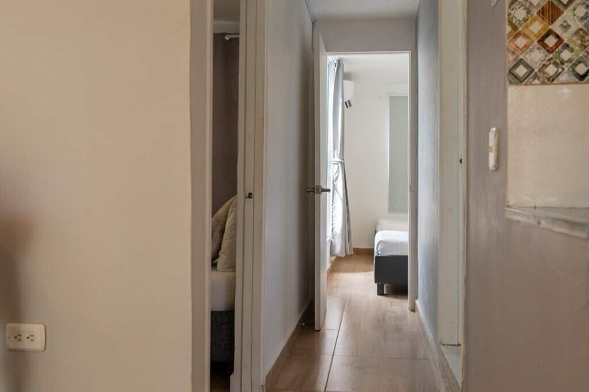 A narrow hallway with a bed at the end, a door on the left, and a tiled wall on the right.