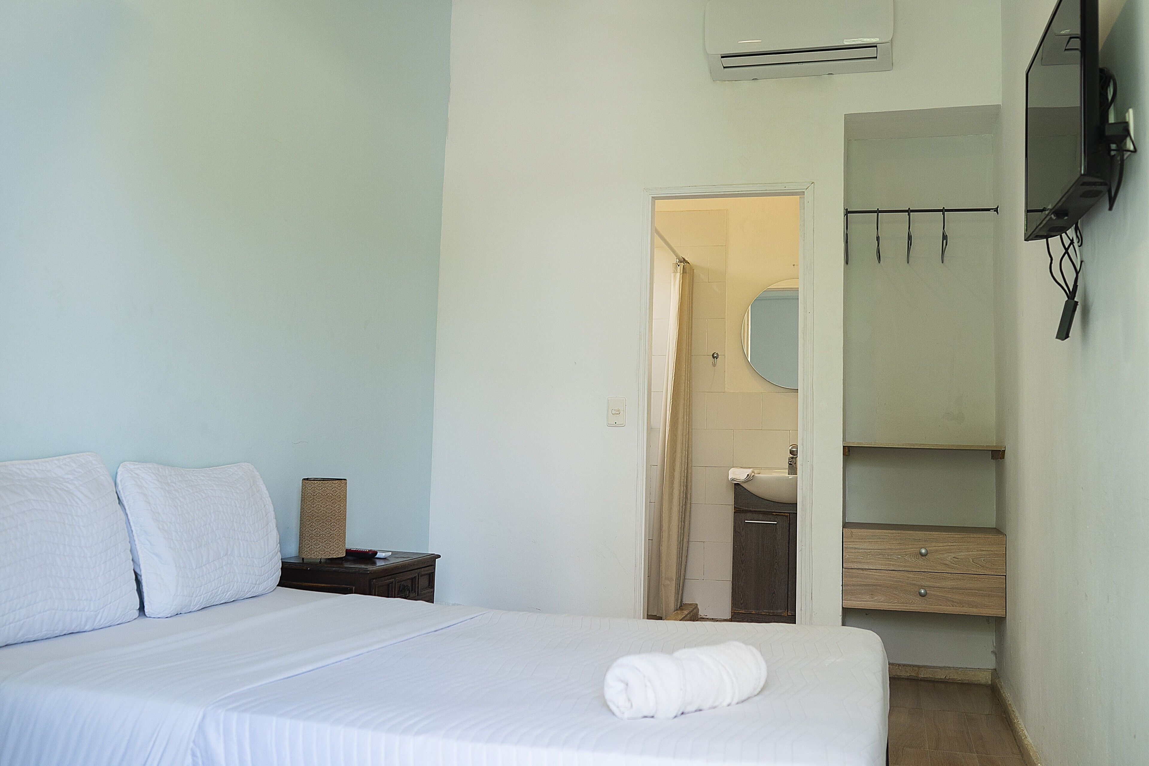 A hotel room with a bed, a nightstand, a mirror, a wardrobe, and an air conditioning unit.