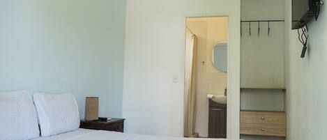 A hotel room with a bed, a nightstand, a mirror, a wardrobe, and an air conditioning unit.
