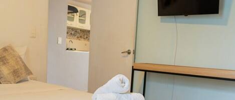 A hotel room with a bed, a folded towel, a television mounted on the wall, and a door leading to a bathroom.