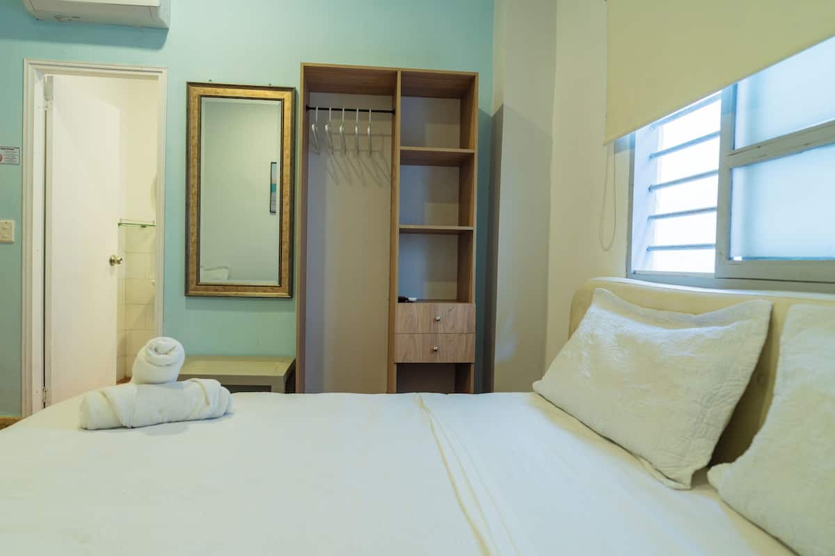 A bedroom with a bed, a wardrobe, a mirror, and a window.