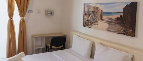 A hotel room with a bed, a desk, a chair, a painting on the wall, and curtains.