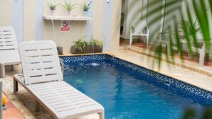 Une piscine avec des chaises longues, des plantes en pot et un panneau indiquant qu’il est interdit de fumer.