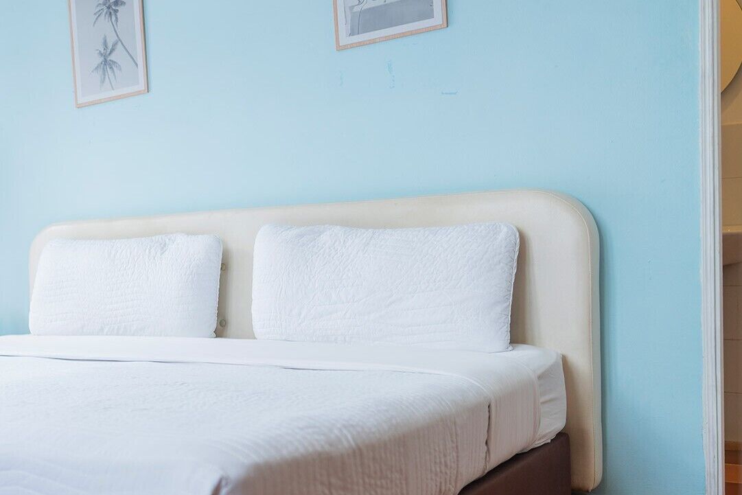 A bed with white bedding, a light blue wall, and two framed pictures.