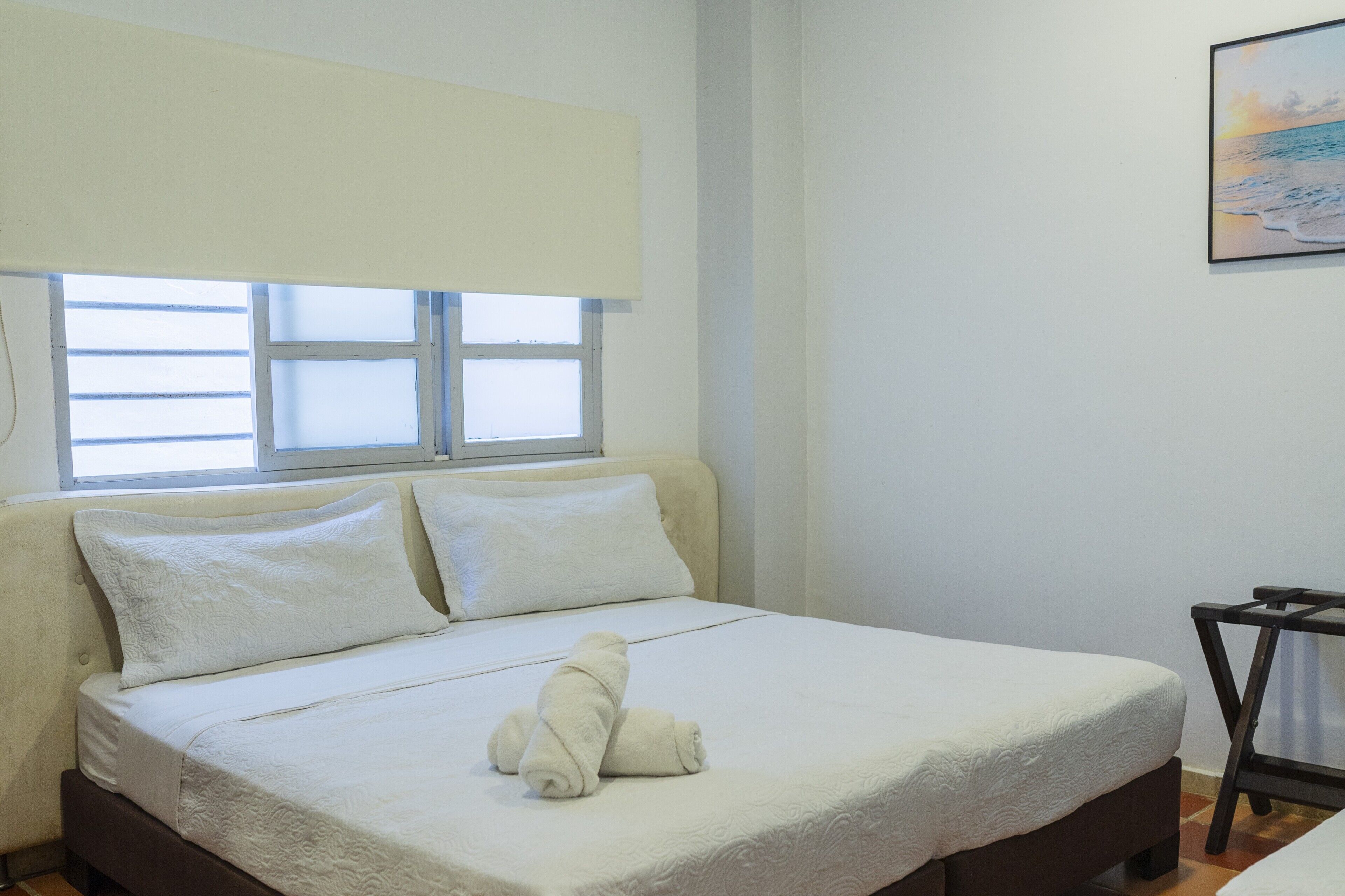 Una cama con una colcha blanca, dos almohadas y una toalla enrollada.