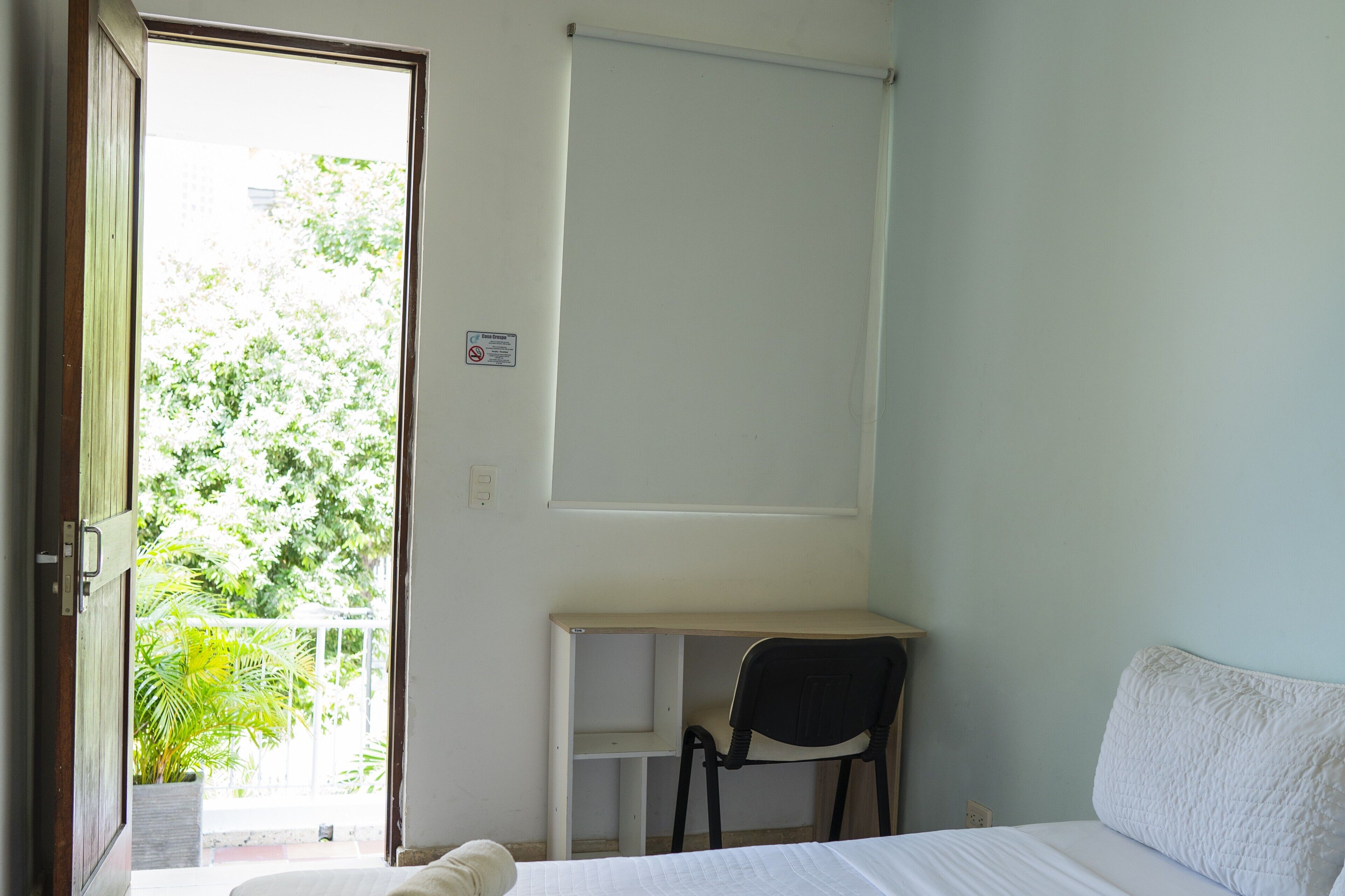 A room with a bed, a desk, a chair, and a window with a view of greenery.