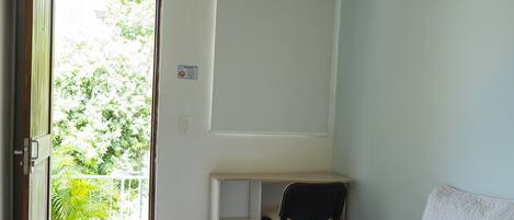 A room with a bed, a desk, a chair, and a window with a view of greenery.