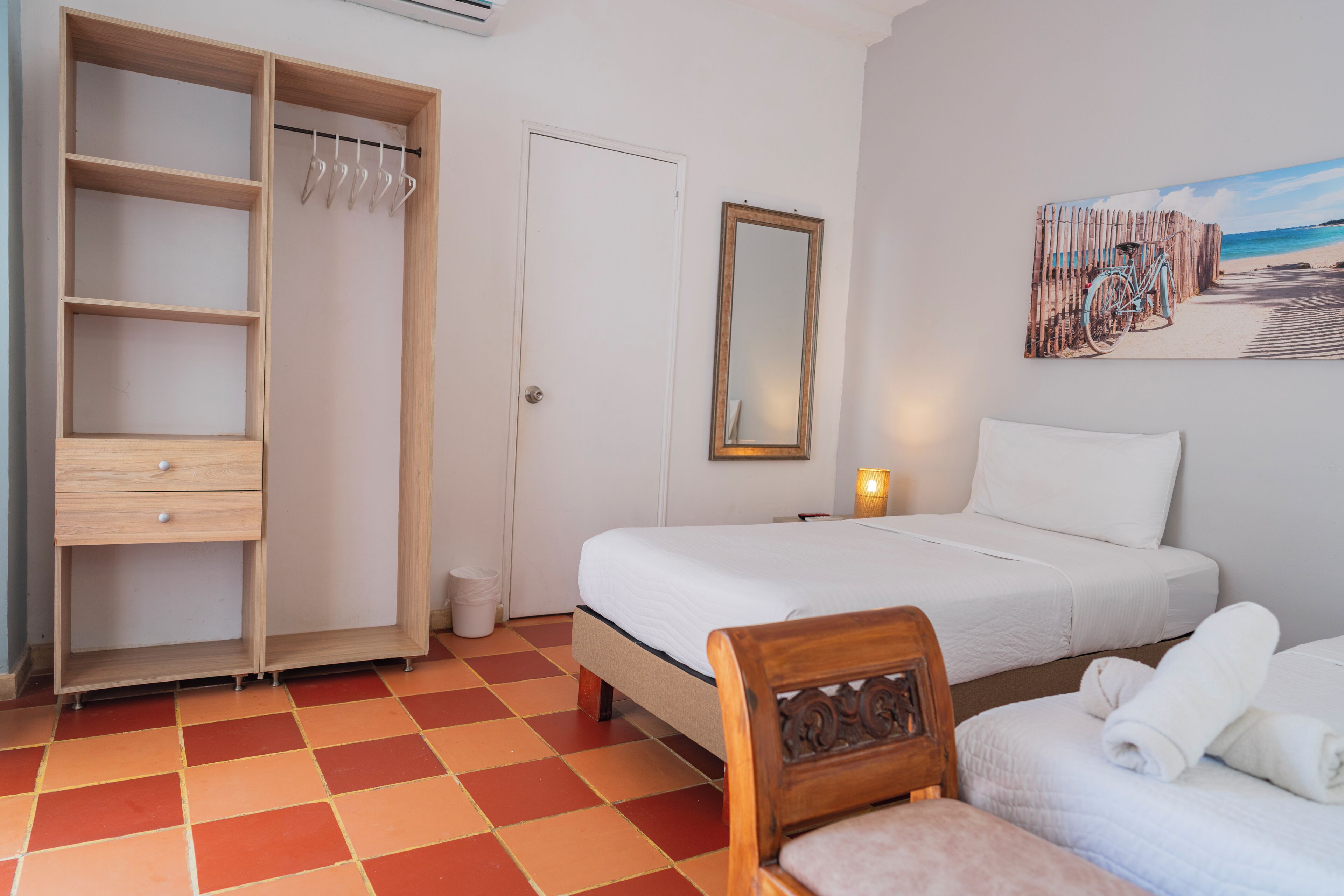 A bedroom with a bed, a wooden wardrobe, a mirror, and a painting of a beach scene.