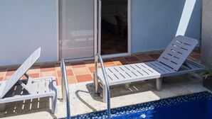 Un espace aménagé au bord de la piscine, avec deux chaises longues blanches et un escalier métallique pour accéder à la piscine.