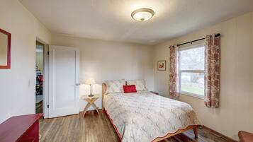 A bedroom with a bed, a nightstand, a lamp, a window with curtains, and a door.