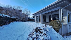 Une maison moderne avec de grandes fenêtres, un porche abrité et une cour enneigée.
