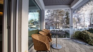 Un espace extérieur abrité, aménagé avec des chaises en osier et une table ronde, d’où l’on peut admirer un paysage enneigé parsemé d’arbres et bordé d’une clôture.