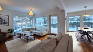 Un salon moderne avec un canapé, une table basse et un coin repas offrant une vue sur des arbres couverts de neige.