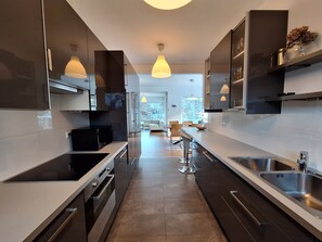 Une cuisine moderne avec des meubles de couleur sombre, des appareils électroménagers en acier inoxydable et des luminaires suspendus.