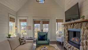 A cozy living room with a stone fireplace, a comfortable sofa, and a television mounted above the fireplace.