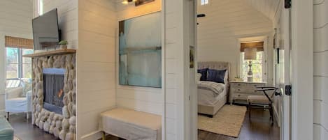 A cozy room with a stone fireplace, a large abstract painting, and a bed with a view of the outdoors.
