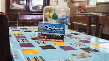 Uma mesa de jantar com toalha de mesa colorida, um recipiente de vidro com objetos decorativos e uma placa com o nome Villa Yudith.