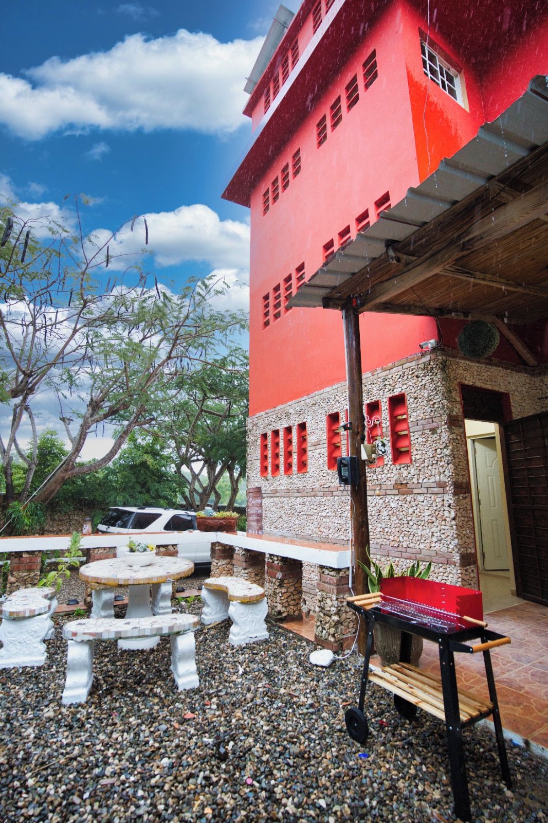 A red building with a stone facade, outdoor seating, and a vehicle parked nearby.