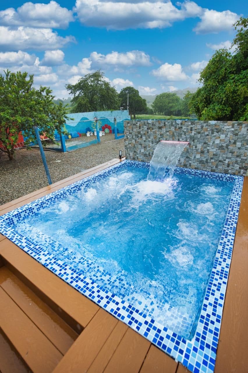 A hot tub with a waterfall feature, surrounded by a tiled deck and a stone wall.