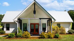A white building with a red door, a covered porch, and a triangular roof. - Sweet Tea Cottage at Julep Farms (Dillard)