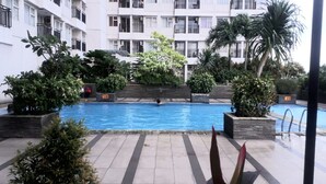 Una piscina rodeada de plantas en macetas y un edificio de varios pisos con balcones.