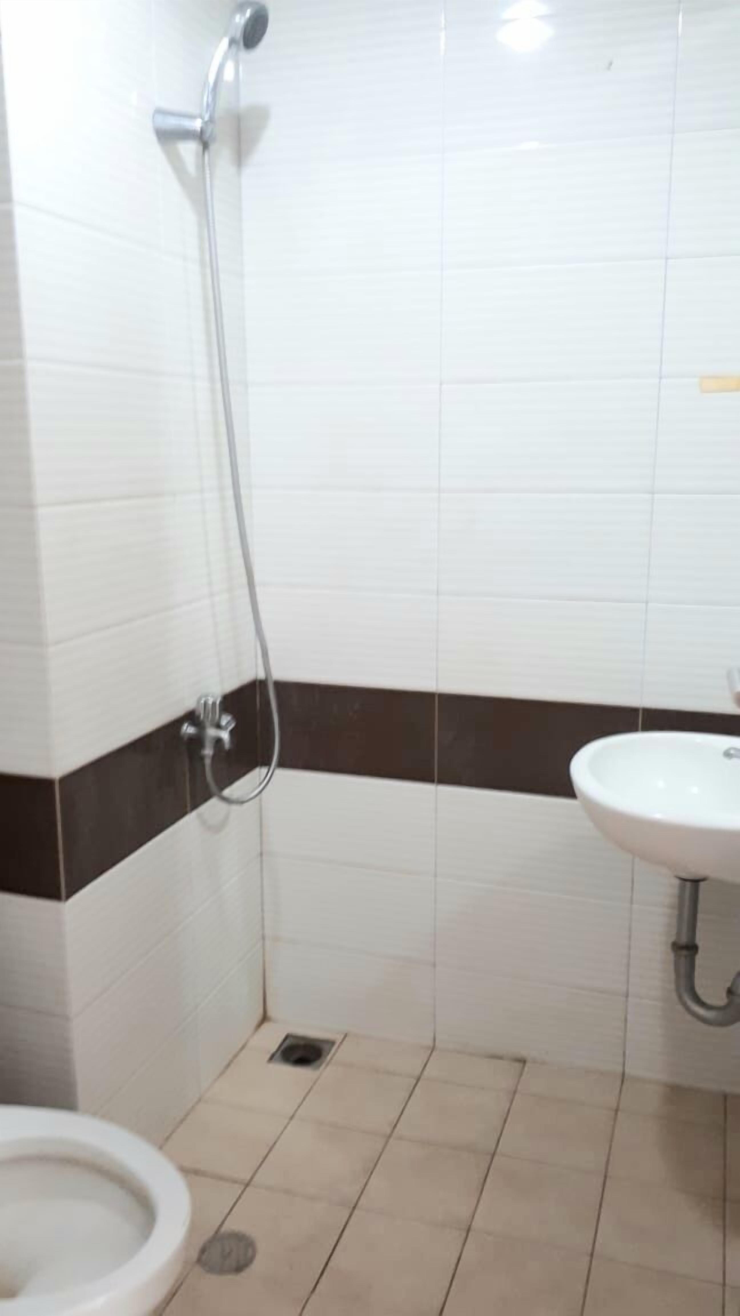 Un baño con paredes de azulejos blancos, una franja marrón, ducha, lavamanos e inodoro.