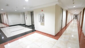 Un largo pasillo bien iluminado con suelo de baldosas, una columna central y puertas a ambos lados.