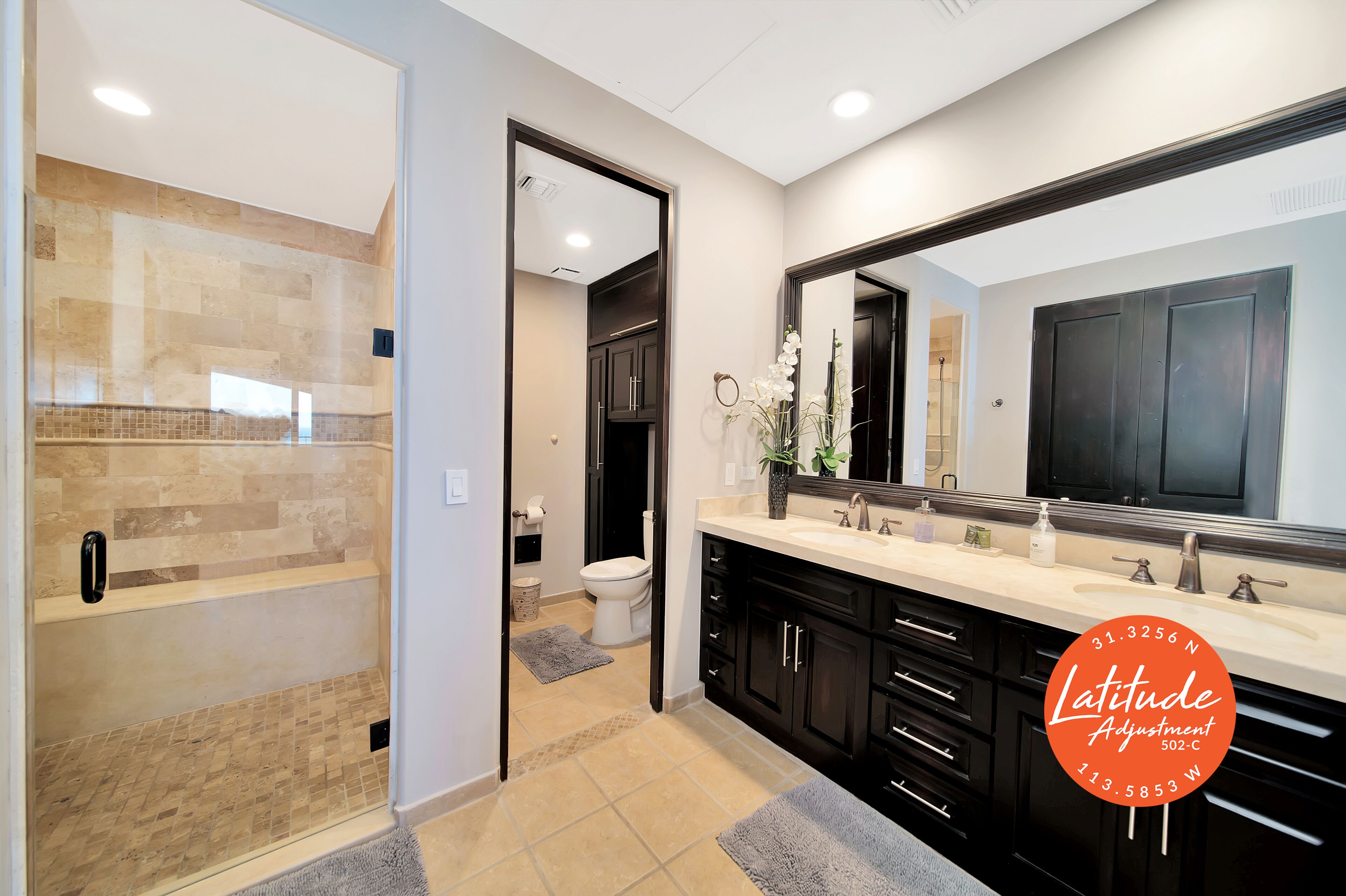 A modern bathroom with a walk-in shower, a large mirror, and a vanity with black cabinets.